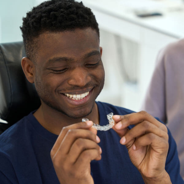 young man smiling and holding clear aligner for teeth